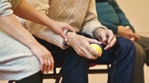Elderly man's arm holding a ball with younger person's arm assisting